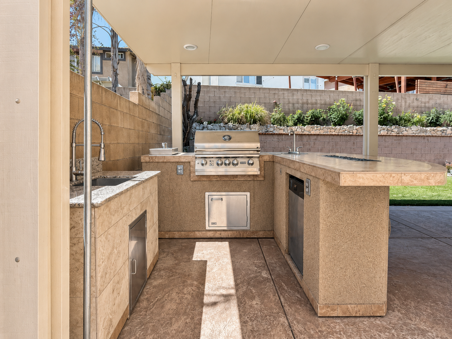Built-in outdoor kitchen island with grill, sink, and bar seating ledge