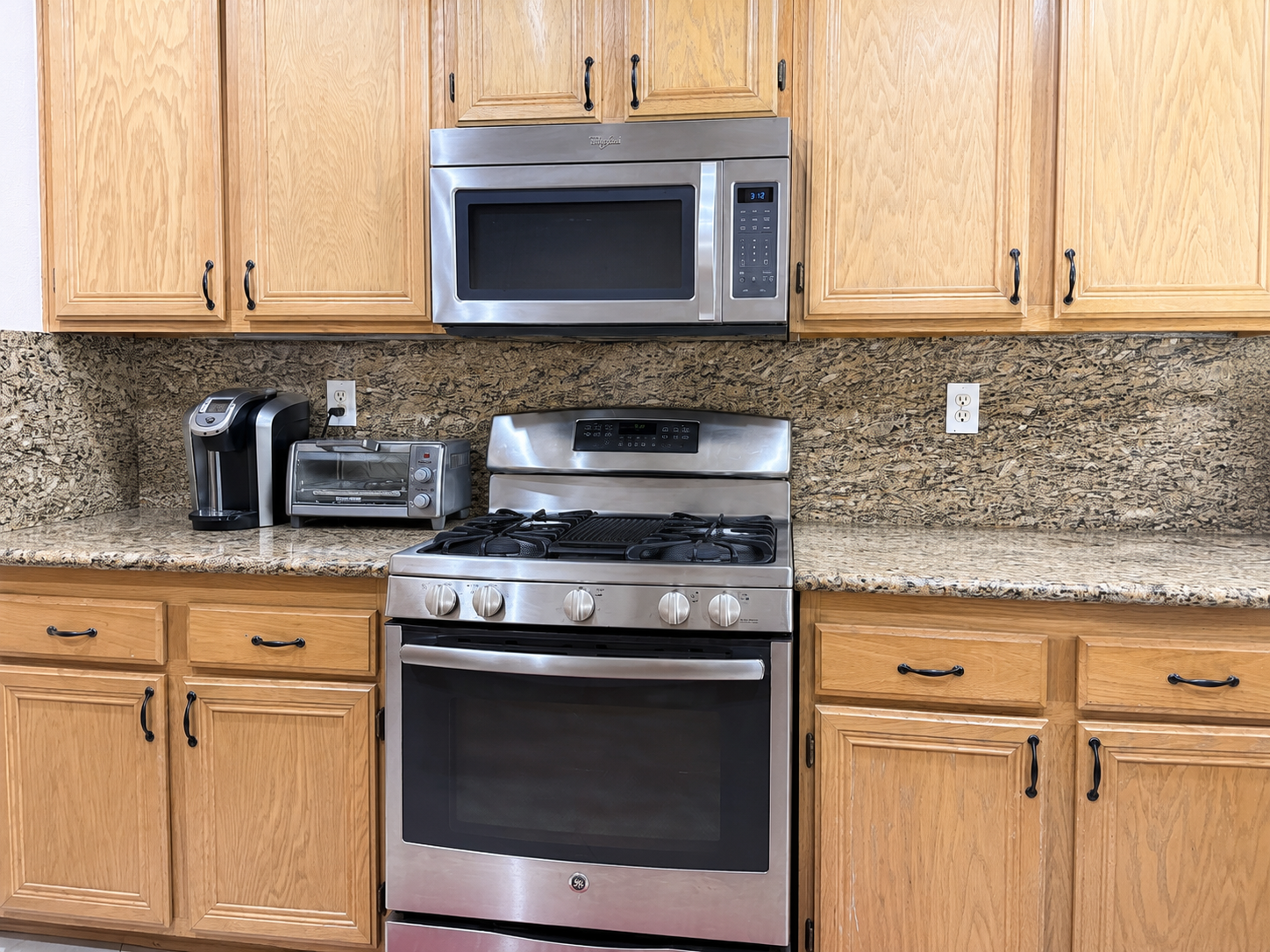 Gas range and stainless-style appliances against the granite backsplash