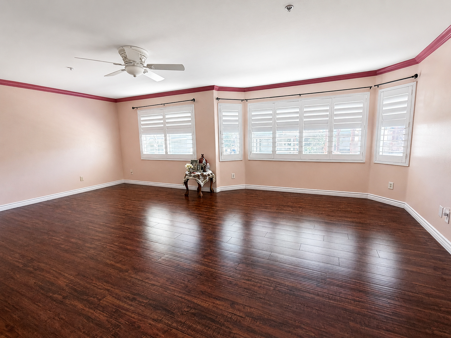 Primary suite with shuttered bay-style windows, ceiling fan, and laminate flooring